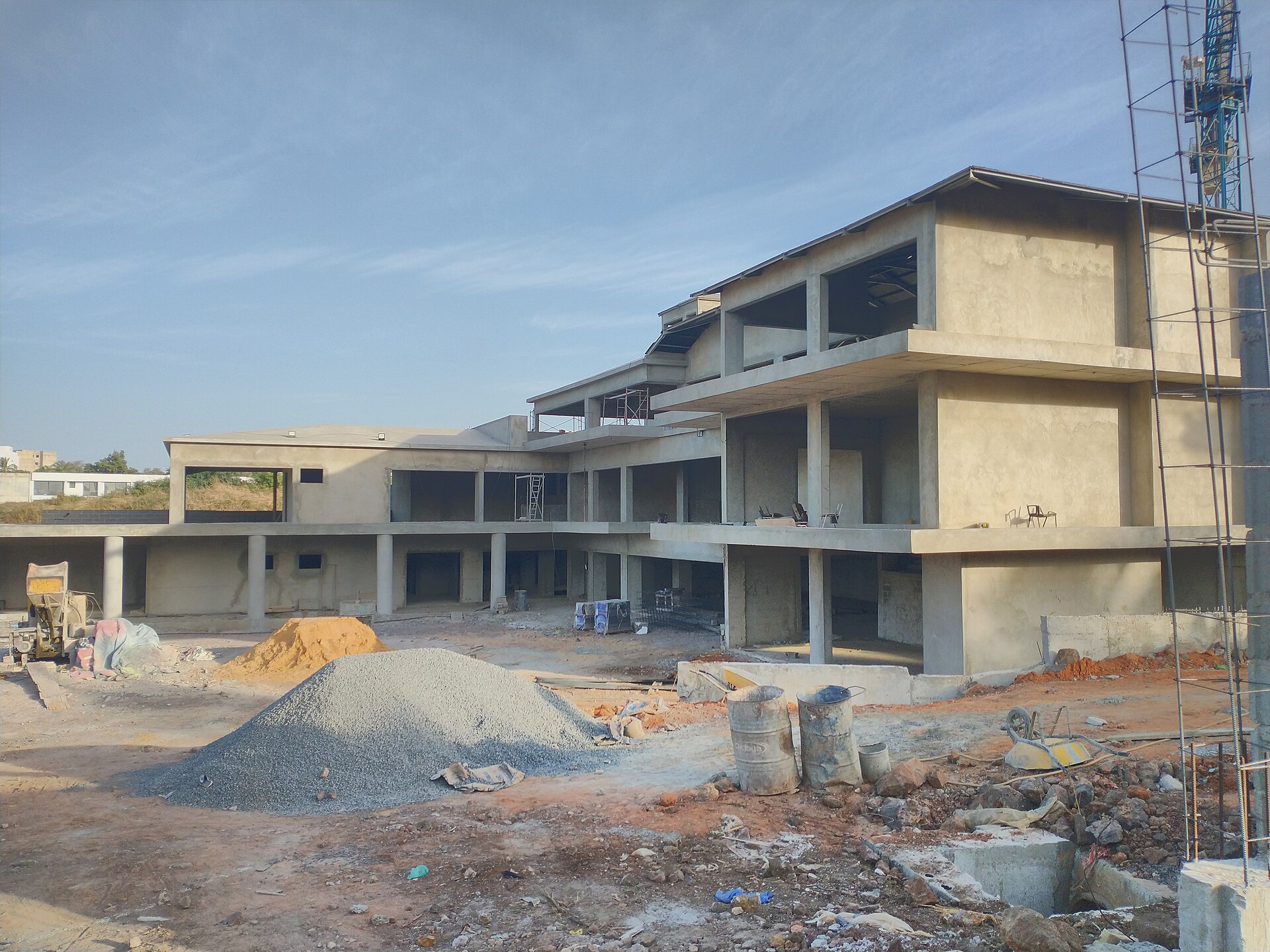 Bâtiment en béton en construction à Mermoz, Dakar, avec des tas de gravier et de sable au premier plan.